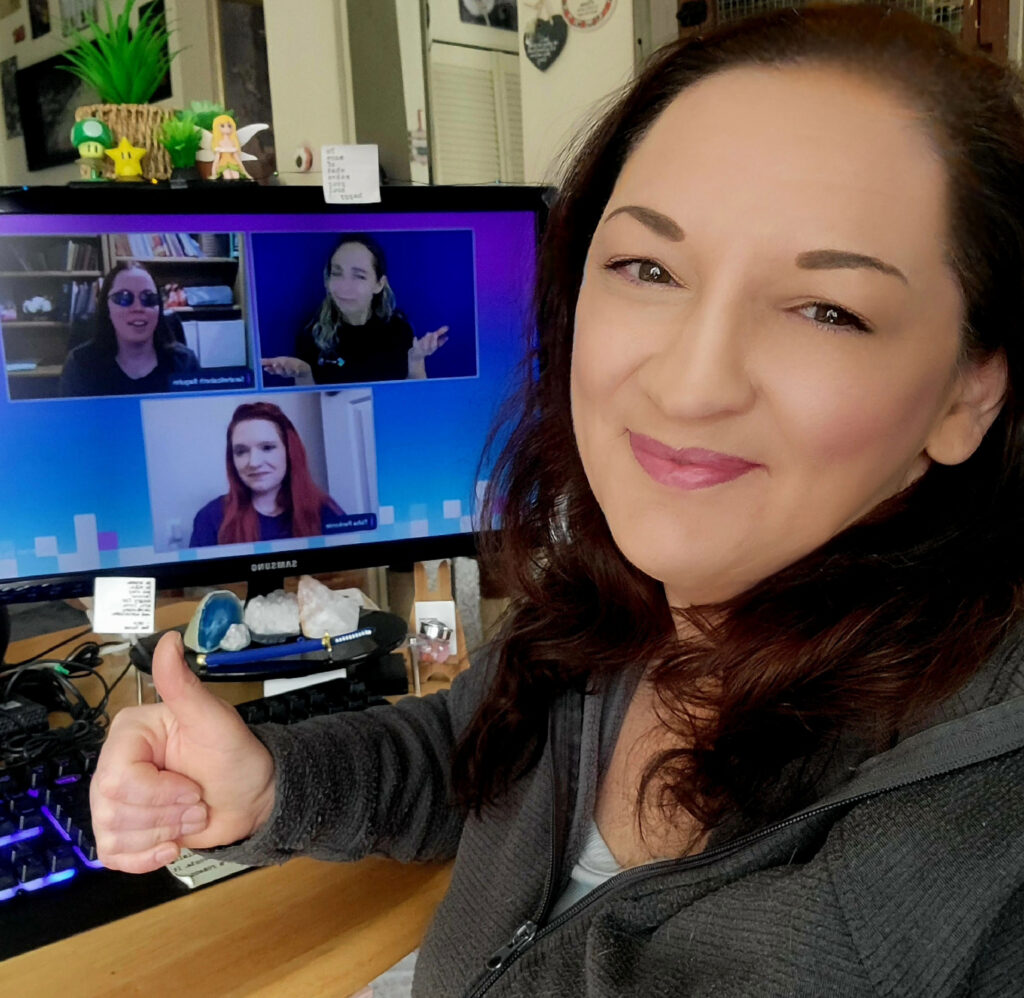 Jaime Hawk sitting in front of her computer giving a thumbs up while attending a virtual accessibility conference.